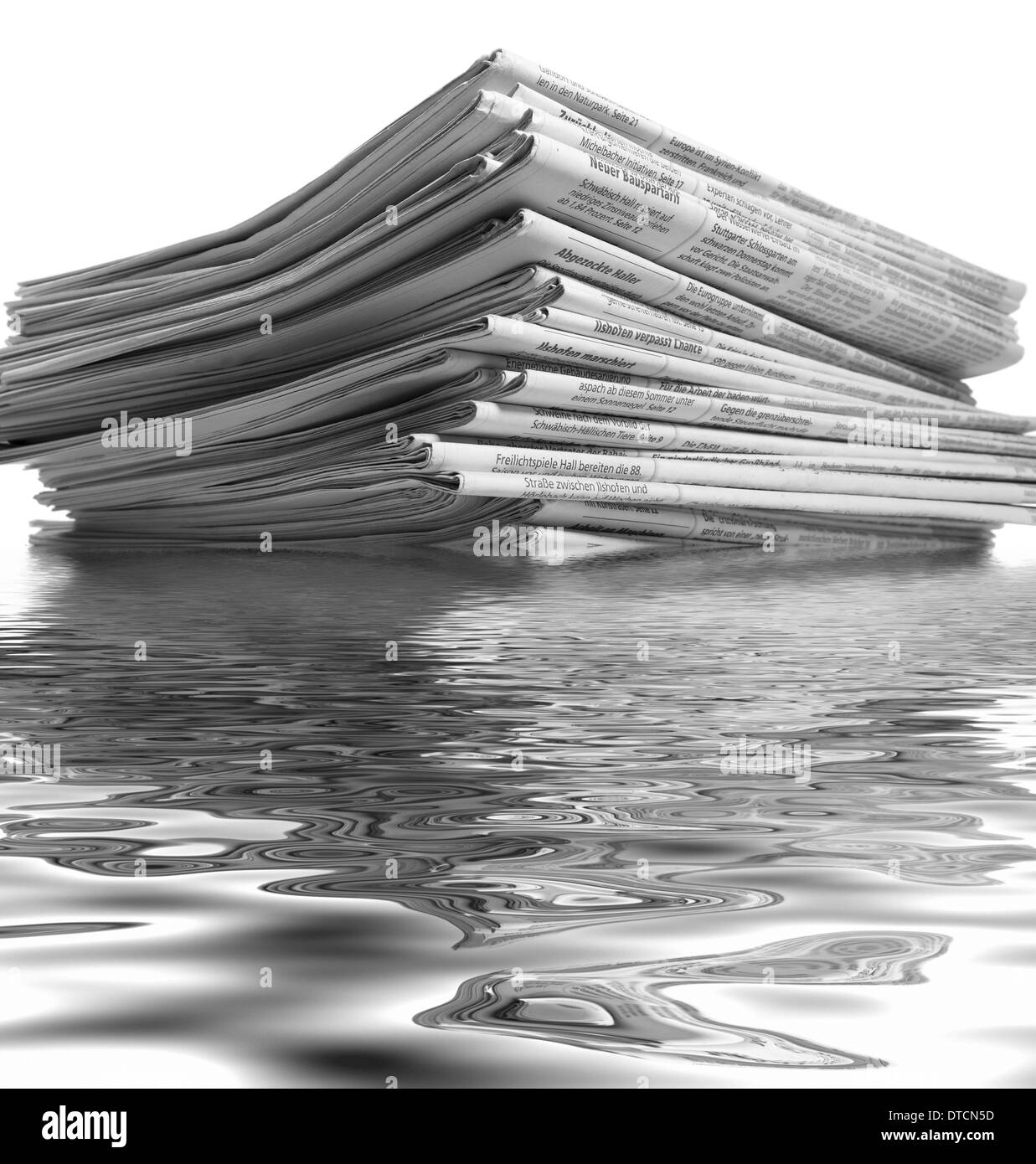 partly sunken stack of newspapers on reflective water surface Stock Photo
