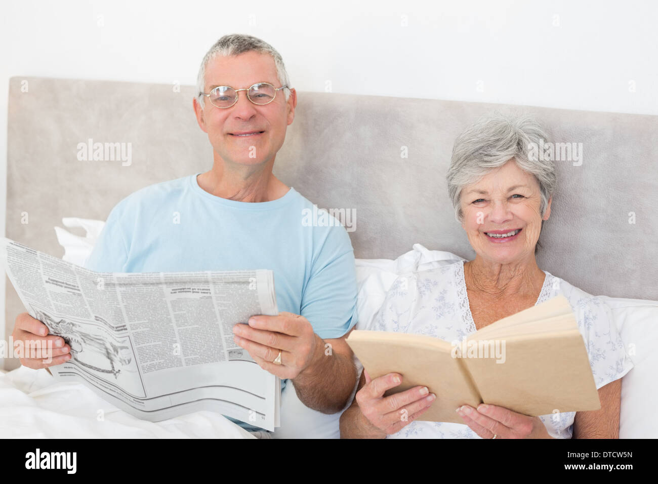 Senior couple holding newspaper and book in bed Stock Photo