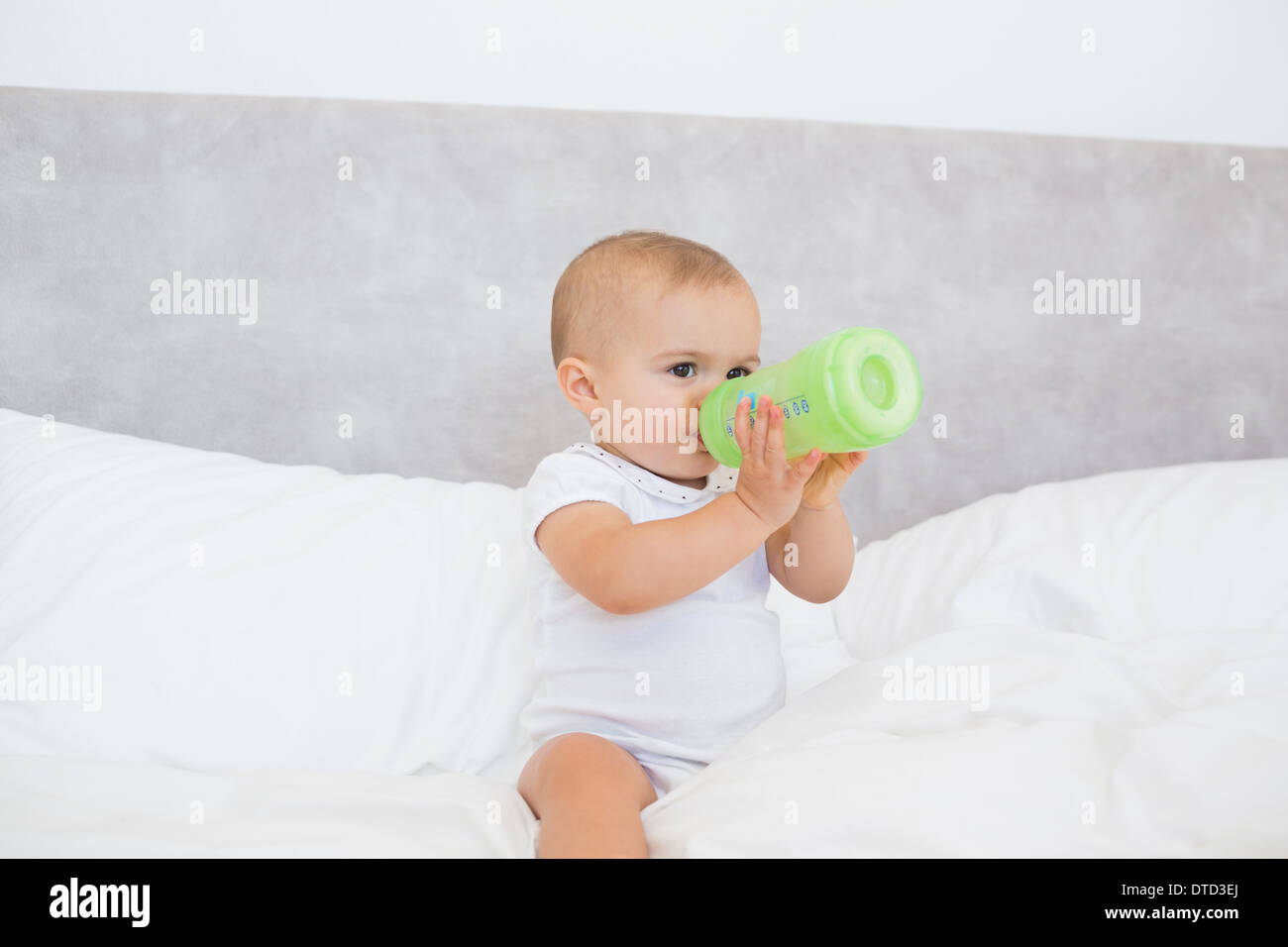 Cute baby with milk bottle sitting on bed Stock Photo