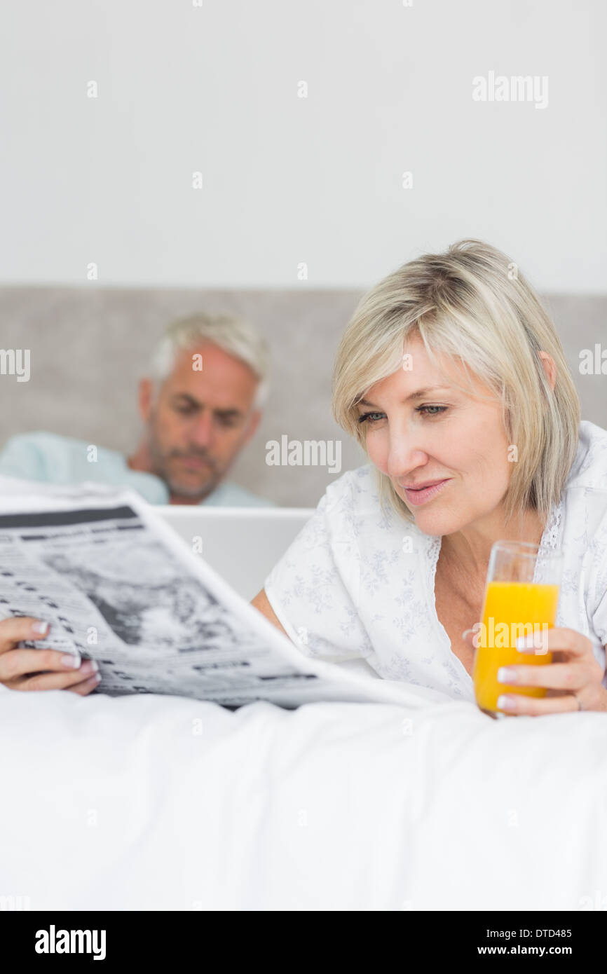 Couple reading newspaper and using laptop in bed Stock Photo
