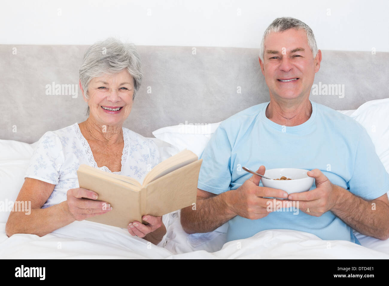 Senior couple with book and bowl in bed Stock Photo