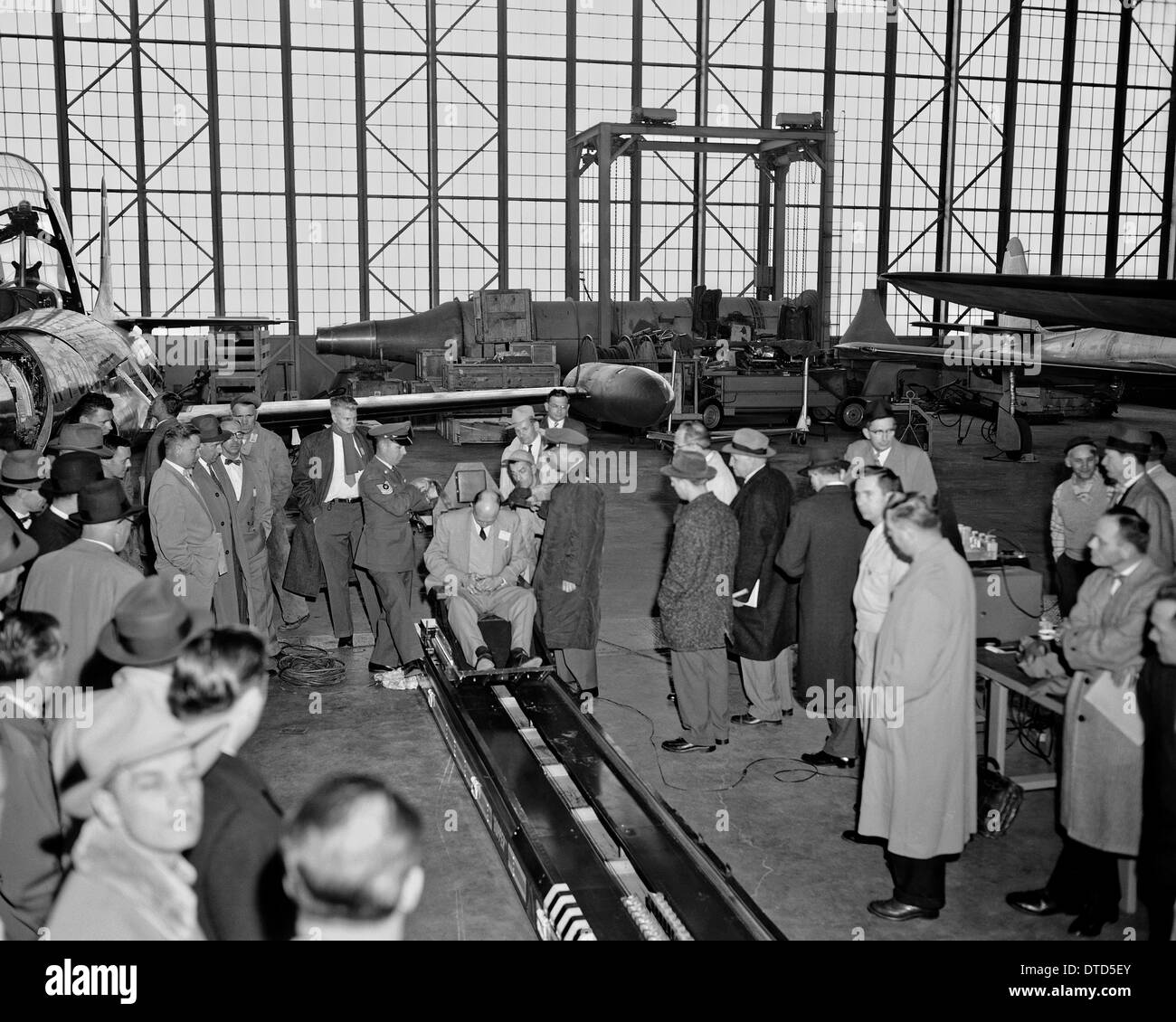 US Army flight surgeon Lt. Col. John Paul Stapp (center) demonstrates the Gee-Whiz rocket sled to a group of dignitaries using Howard Hasbrook as the demonstrator sitting in the machine April 17, 1956 at Edwards Air Force Base, CA. Stock Photo