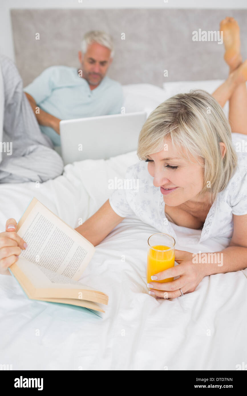 Couple reading book and using laptop in bed Stock Photo