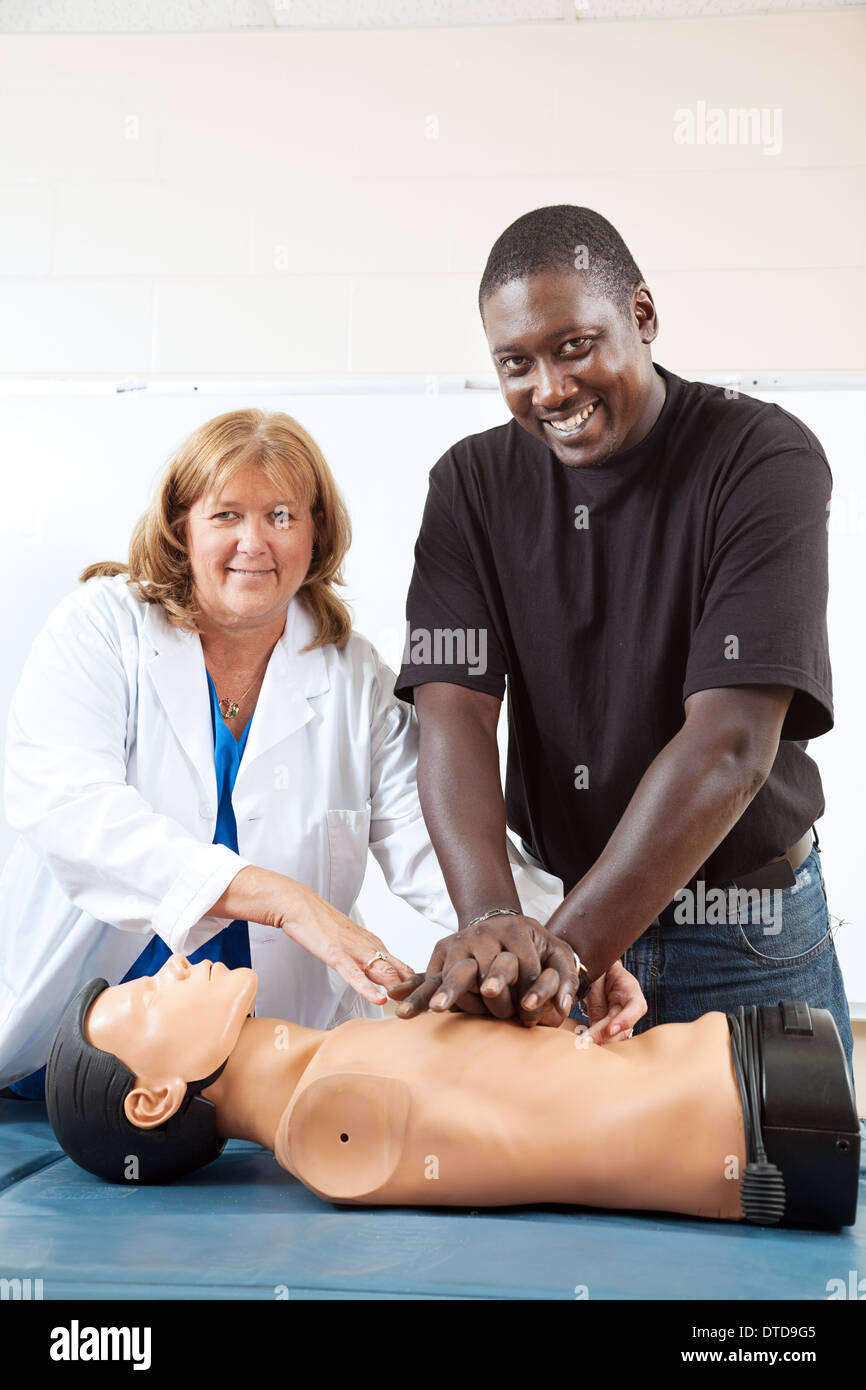 Adult first aid or EMT student practicing CPR on a dummy, with the help of a doctor or nurse. Vertical with room for text.  Stock Photo