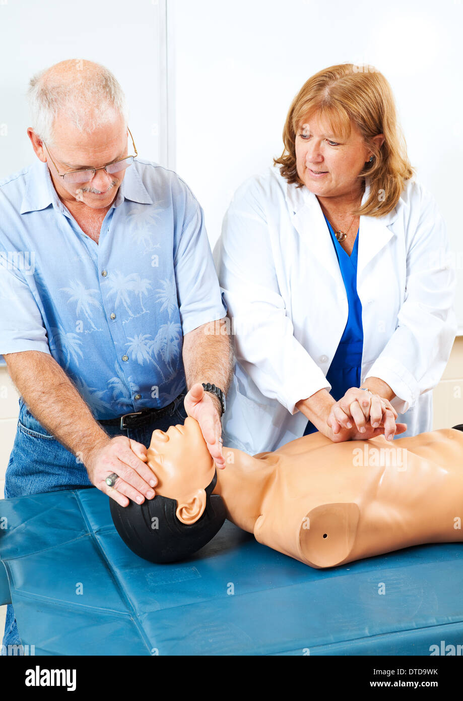 Doctor teaching first aid CPR to a mature adult student using a mannequin. Stock Photo