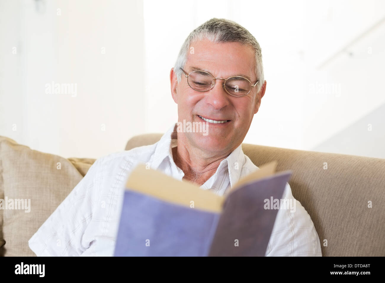 Senior man reading book on sofa Stock Photo