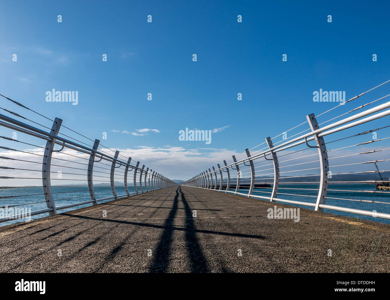 Handrails and shadows on a breakwater recede into the distance. Stock Photo