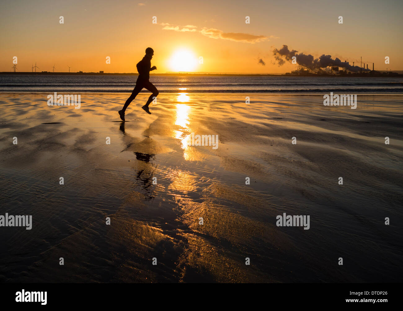 Man running on North Gare beach at sunrise.Redcar Steelworks in on the south side of the Tees estuary, Teesmouth in background. England. UK Stock Photo