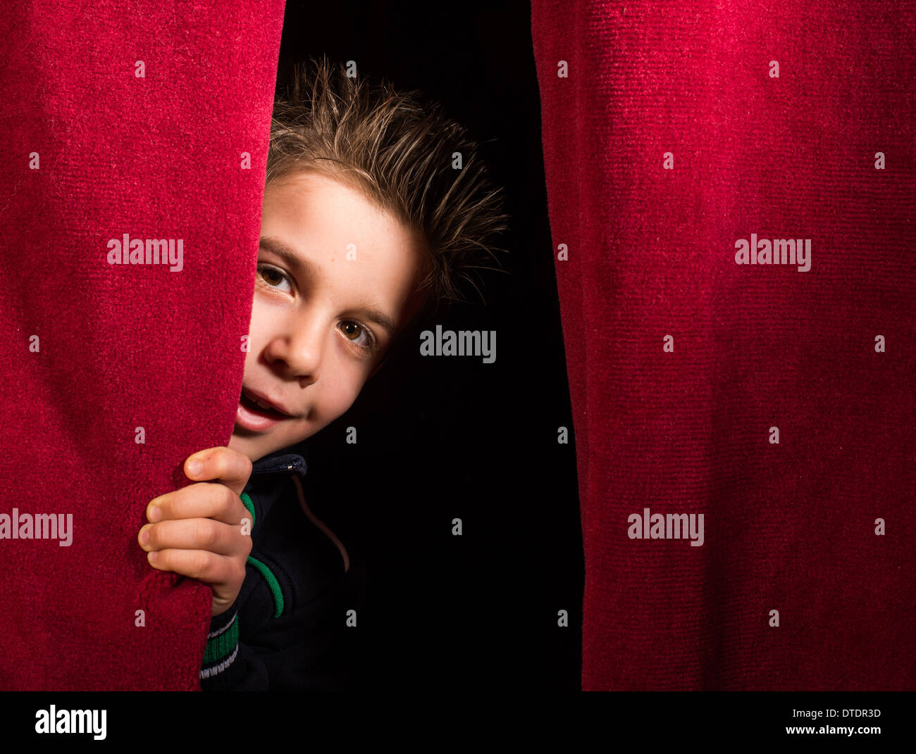 Child appearing beneath the curtain. Red curtain. Stock Photo