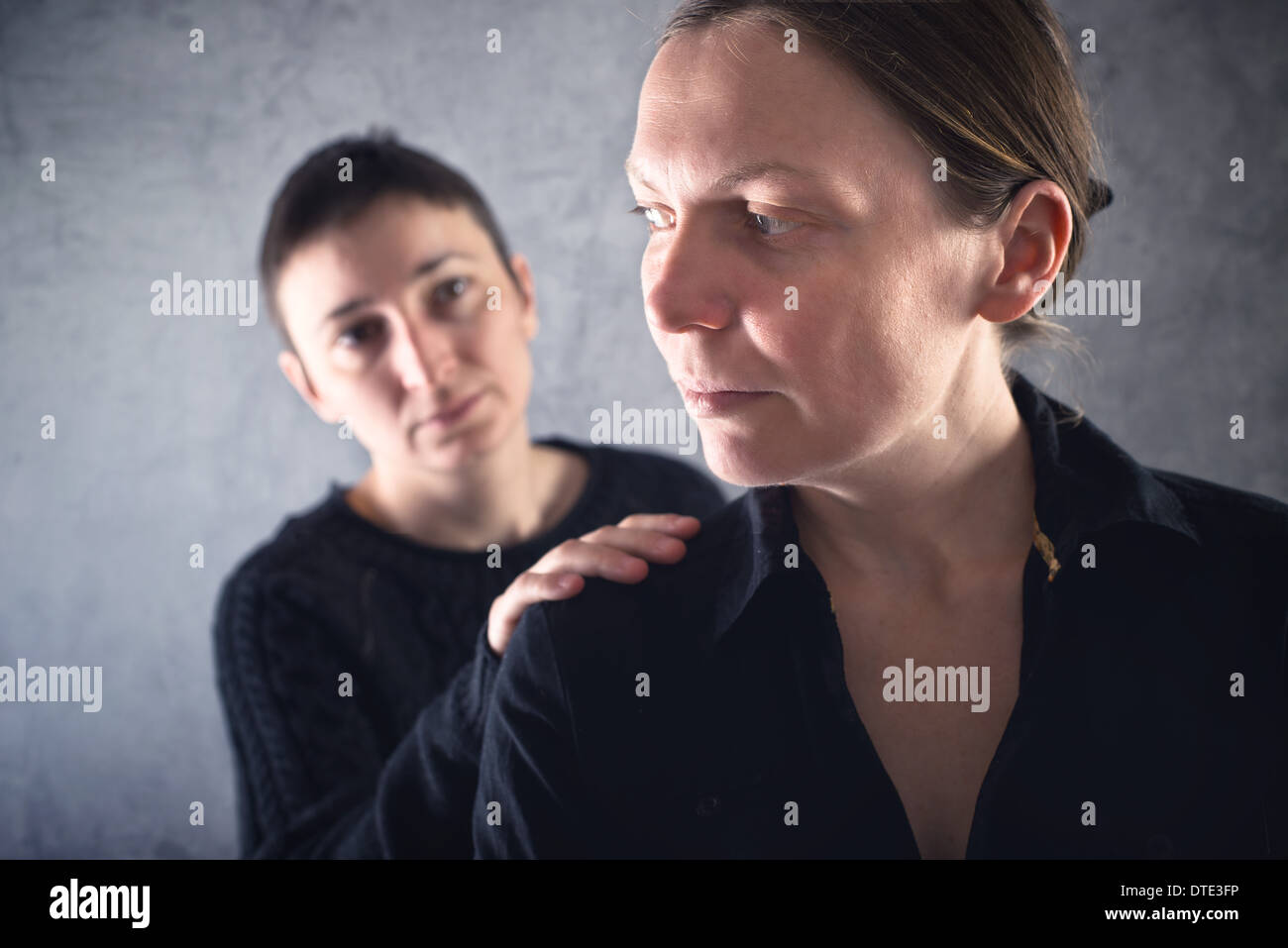 Comforting friend. Woman consoling her sad friend with hand on shoulder. Stock Photo