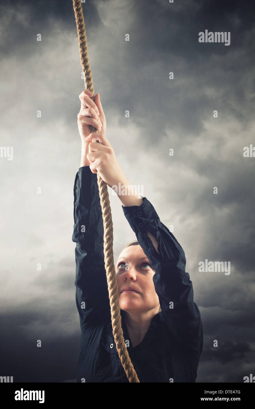 Woman climbing up with rope. Overcoming problems, obstacles and difficulties in life metaphor. Stock Photo