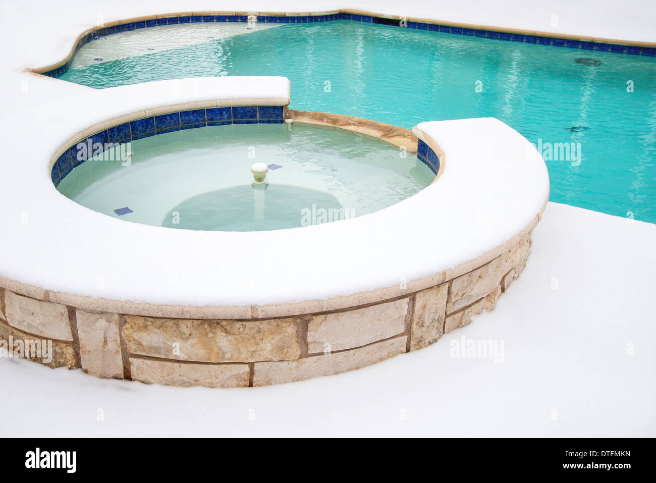 Outdoor hot tub or spa by swimming pool surrounded by snow in the winter Stock Photo