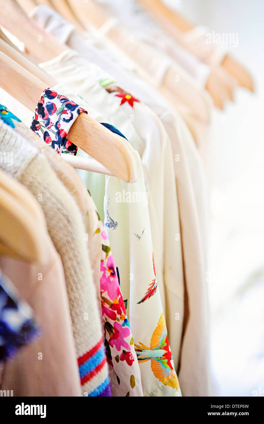 Light colored blouses with pops of color and floral motifs on wood hangers Stock Photo