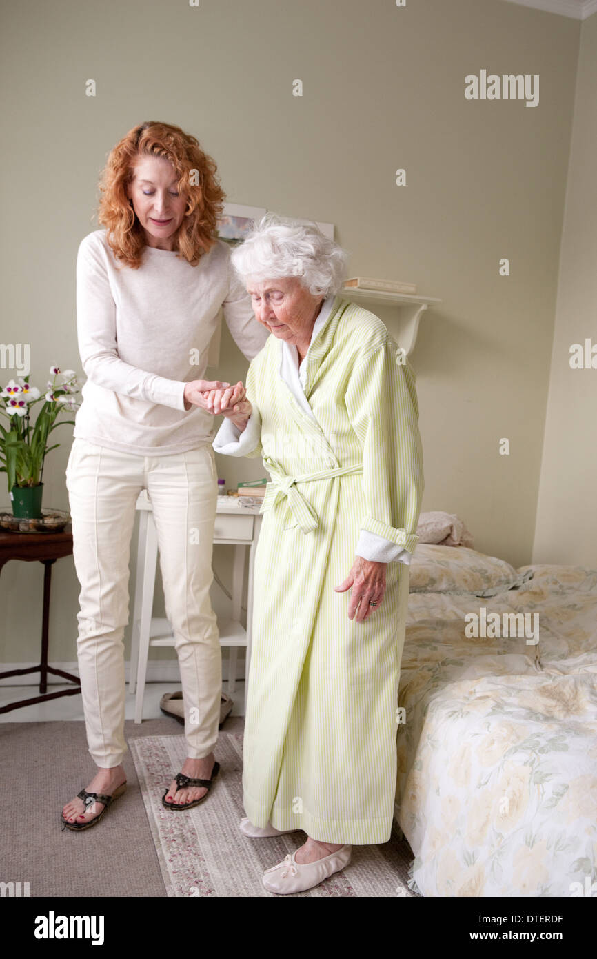 Female caregiver helping elderly woman get out of bed Stock Photo