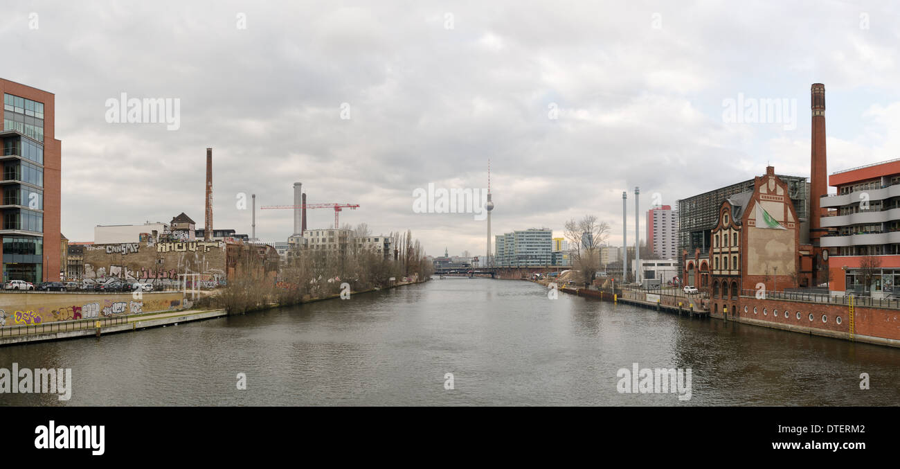 Looking westward to the Berlin TV tower on bridge over river Spree overcast doom and gloom reflection in calm waterway industry Stock Photo