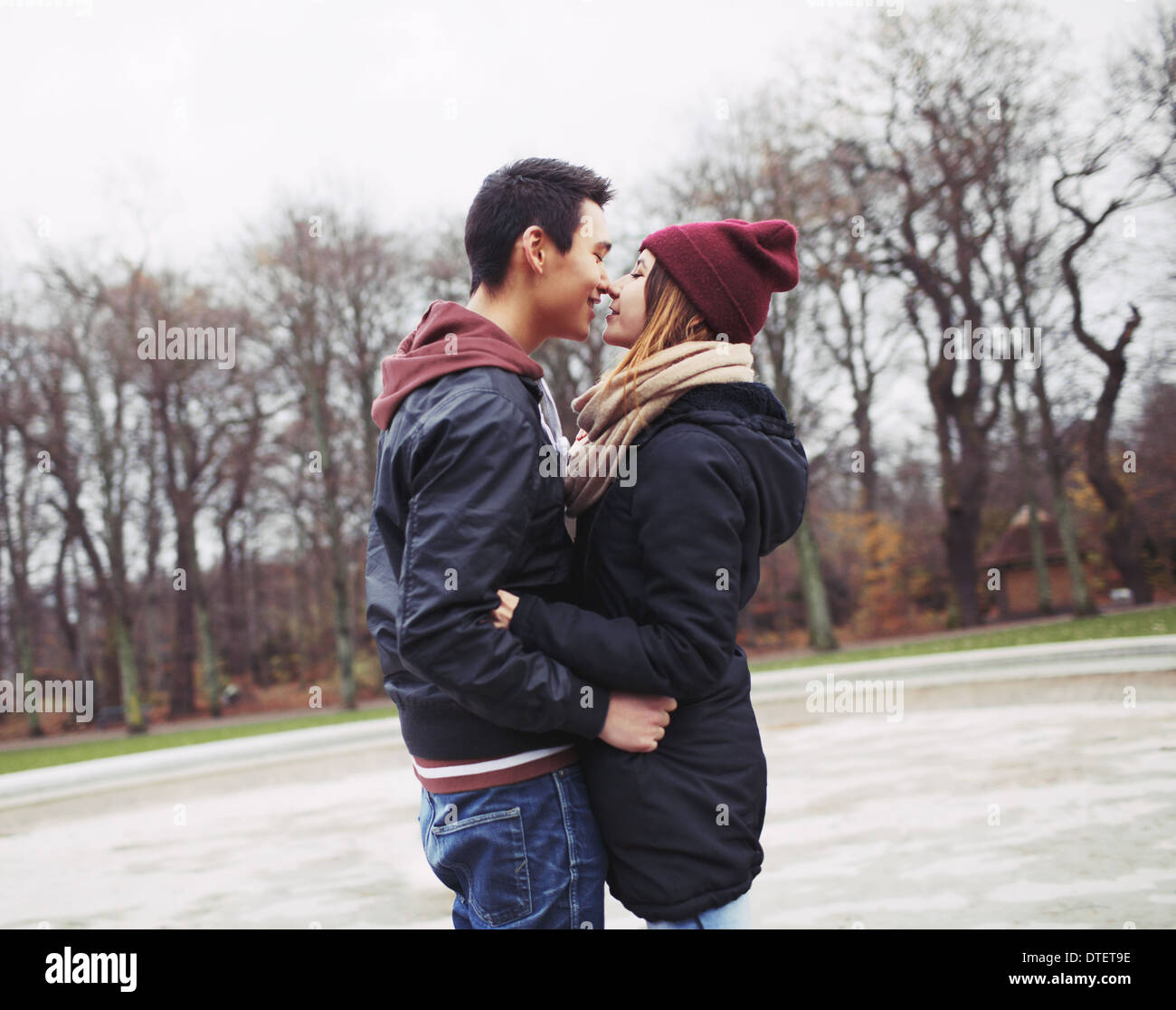 Mixed race teenage couple about to have a passionate kiss in park. Handsome young man and beautiful young woman in warm clothes. Stock Photo