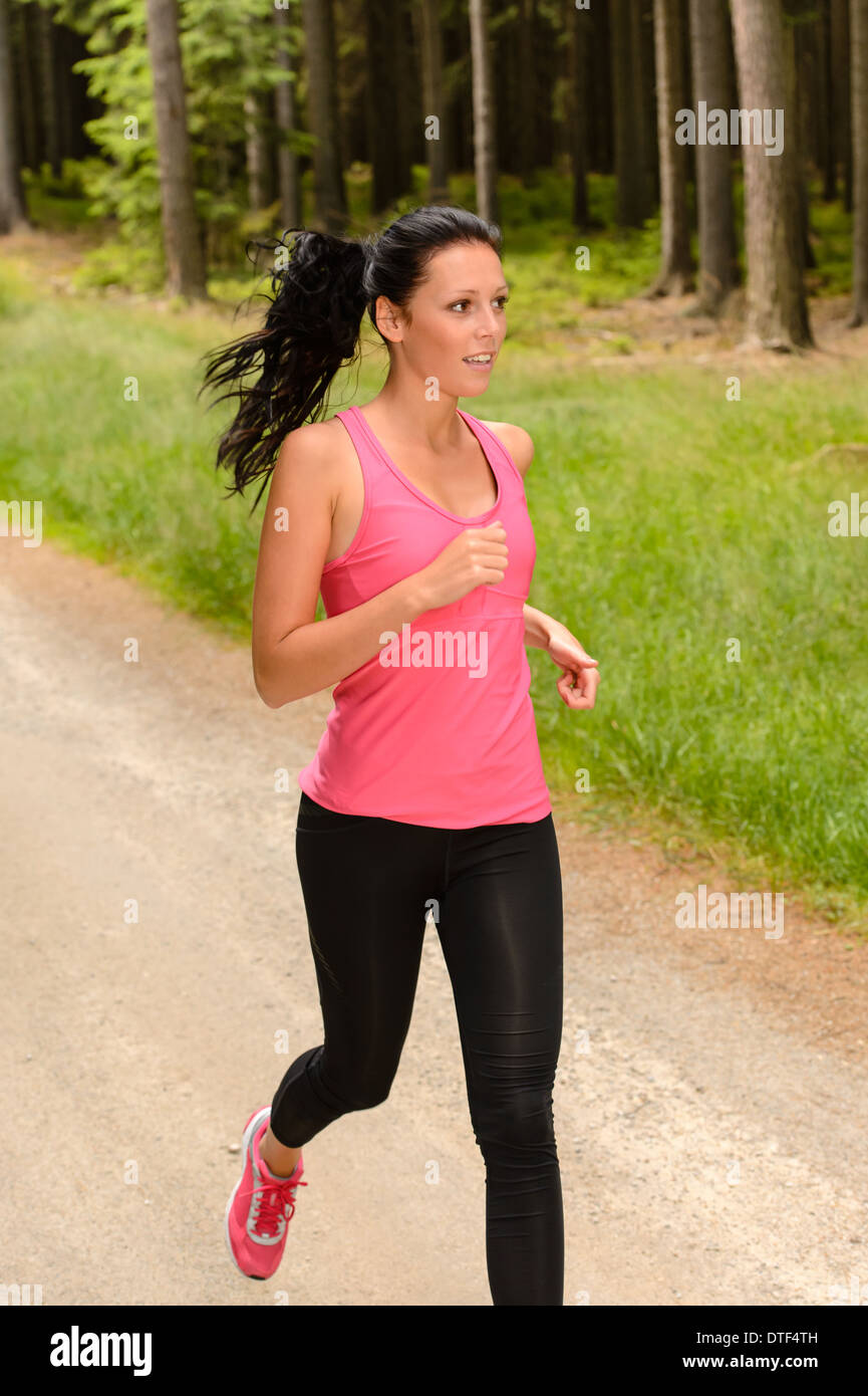 Sportive woman running through forest on summer training day Stock Photo