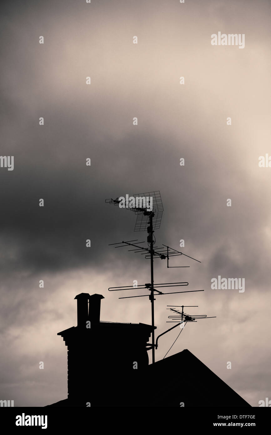Silhouette of rooftop, chimney and antenna of old house with dark, mysterious and moody setting Stock Photo