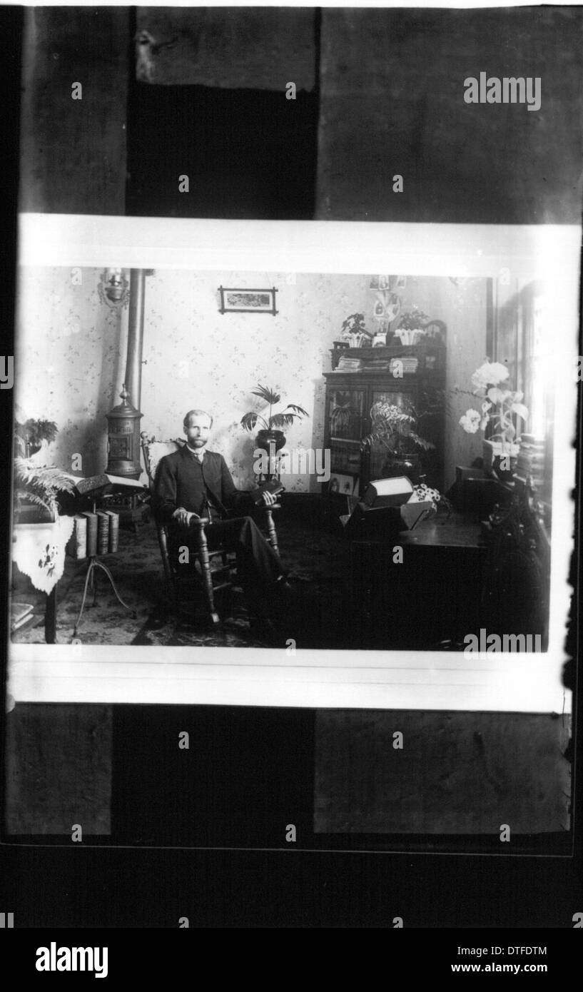 This historical photograph from the Miami University digital collections shows a man seated in a rocking chair, likely taken in Oxford, Ohio. The image is part of a series of interior portraits, offering a glimpse into the everyday life of the past. Stock Photo
