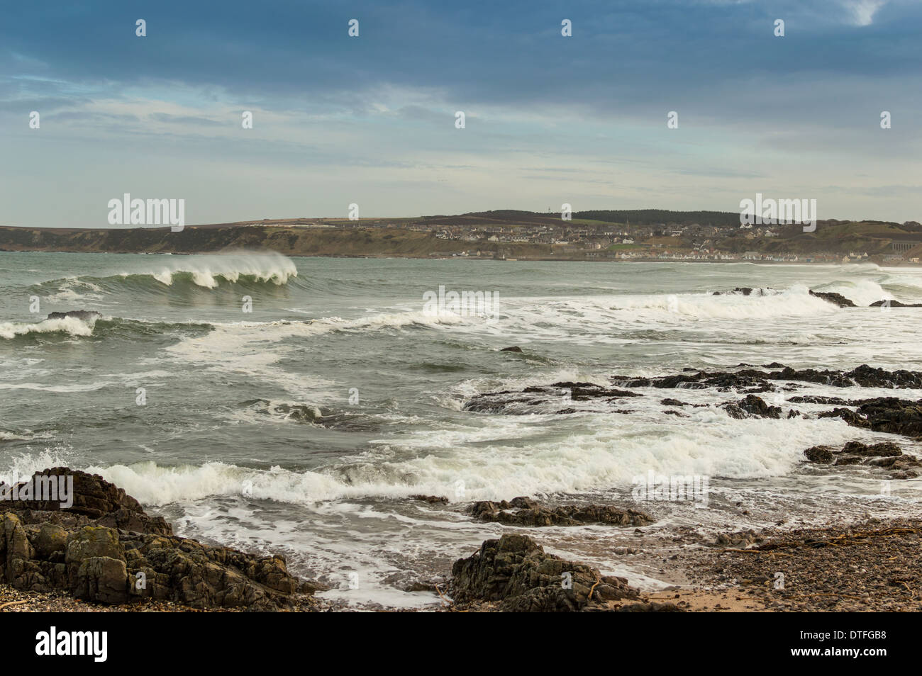 WAVES BREAKING ON THE SHORE AT CULLEN BAY MORAY WITH CULLEN TOWN IN THE DISTANCE Stock Photo