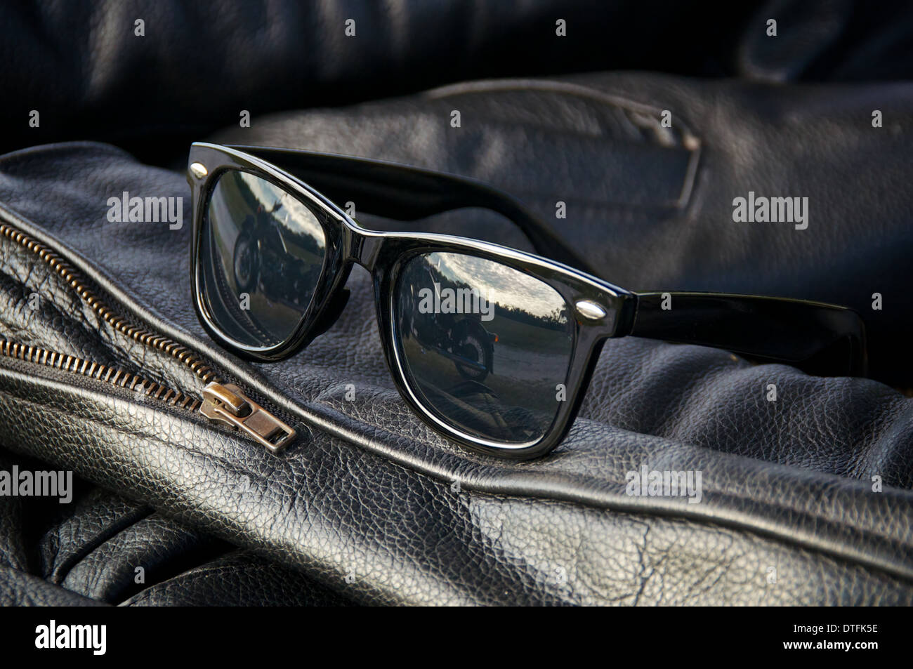 close up generic wayfarer sunglasses on sleeve of buffalo hide motorcycle  jacket showing motorcycle in reflection Stock Photo - Alamy