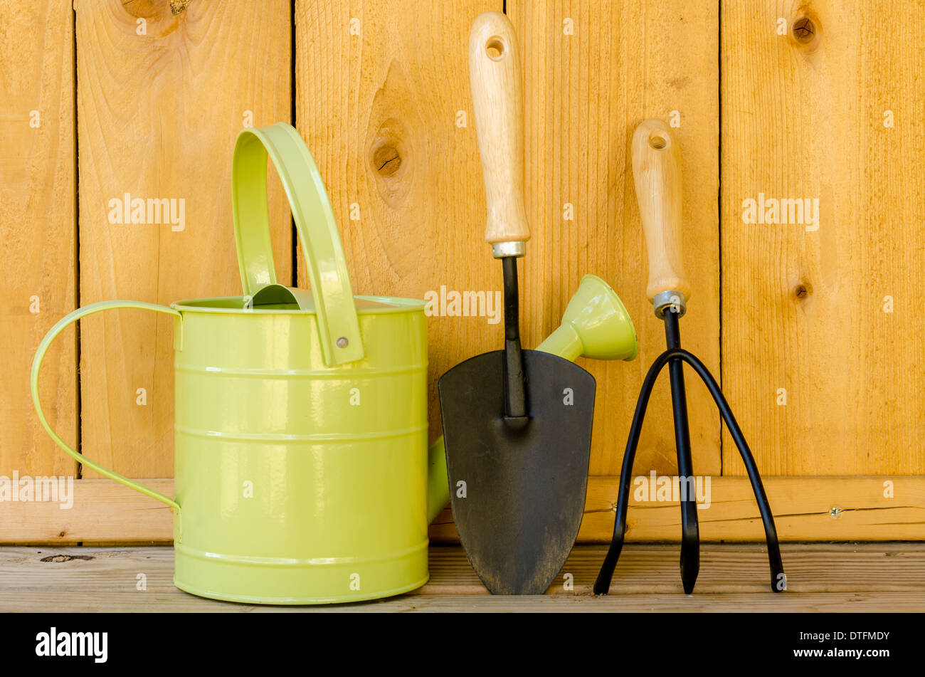 Gardening tools with watering can, trowel, and hand cultivator on wood background. Stock Photo