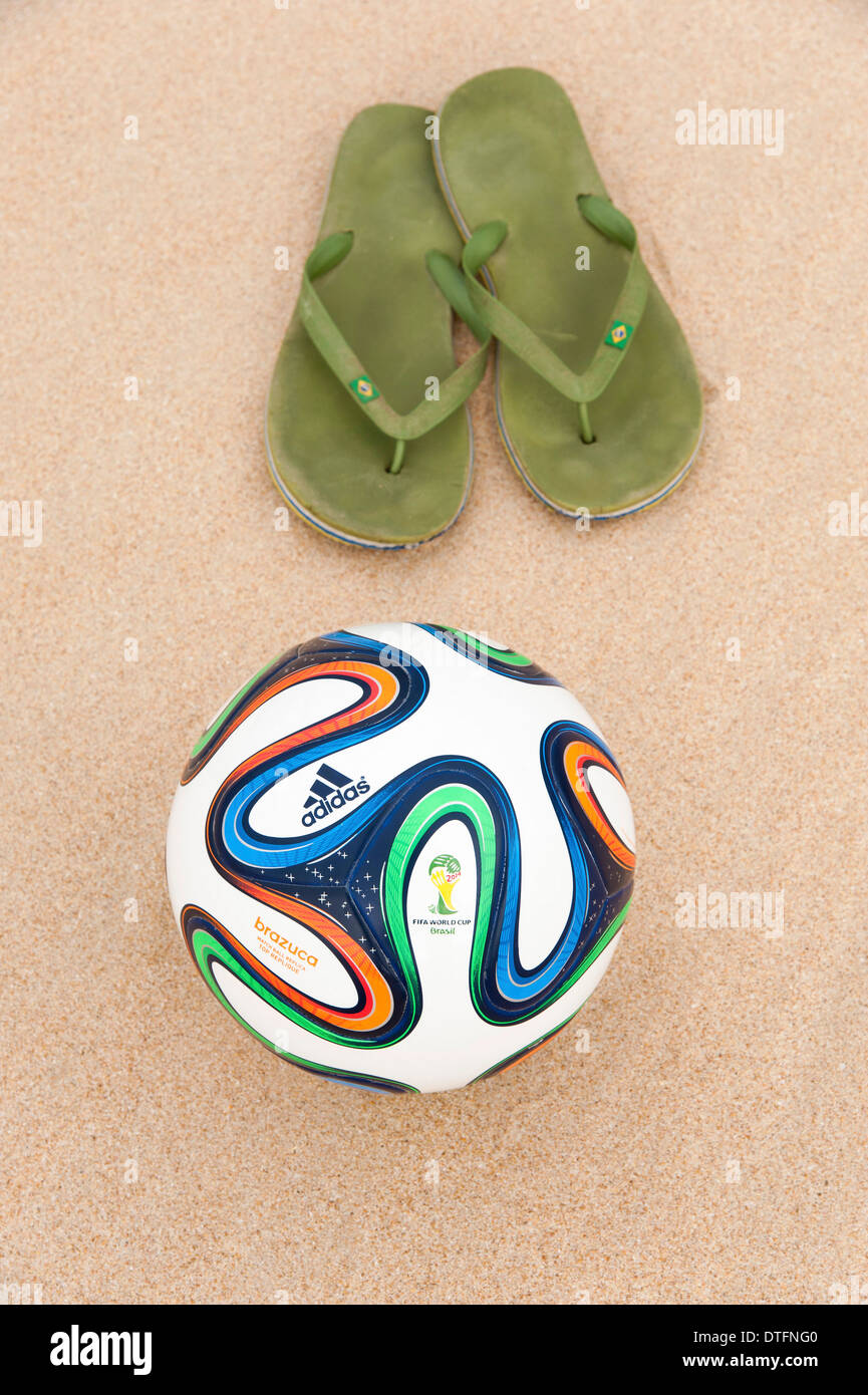 Brazuca (replica), official match ball of the FIFA World Cup 2014 in Brazil in the sand next to worn out green flip-flops Stock Photo