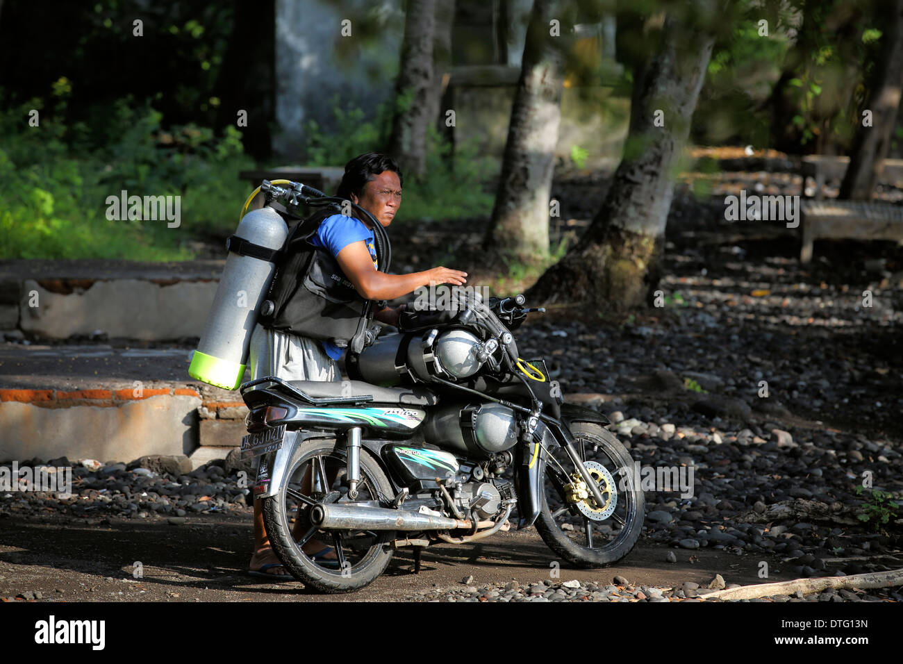 Balinese man carries scuba diving tanks to the beach on a motor scooter Stock Photo