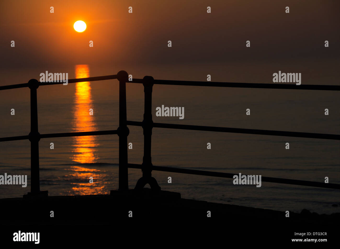 The sun rising behind the promenade barrier at Eastbourne in Sussex, England, UK Stock Photo