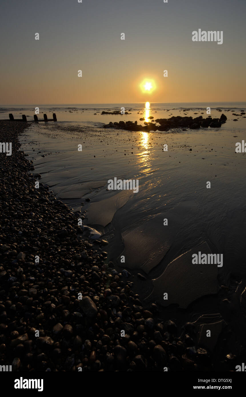 Sun rising over the sea at Eastbourne in Sussex, England, UK showing reflection in wet sand and seacolor Stock Photo
