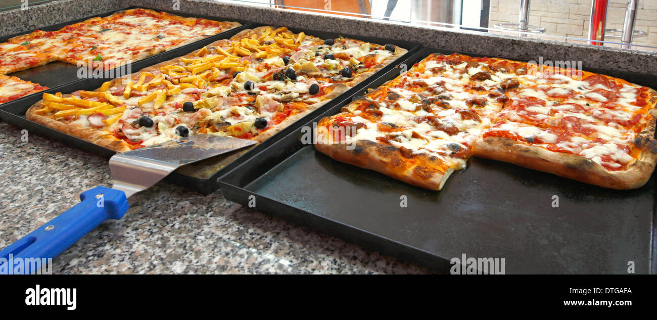 Counter of the pizzeria with trays and square pieces of pizza. Stock Photo
