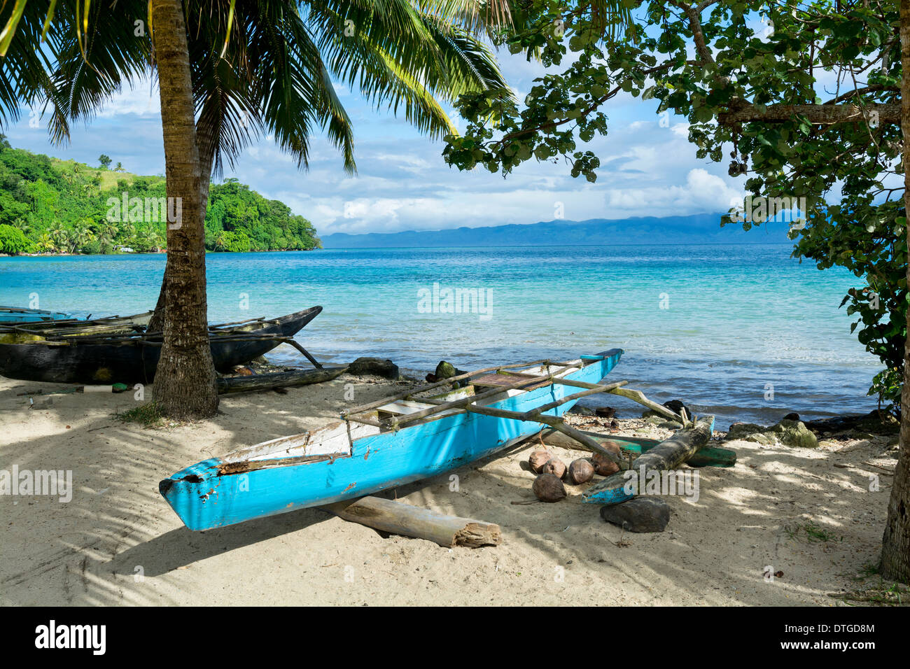 A blue Polynesian outrigger that's still used today rests on the shore of a tropical island in Fiji Stock Photo