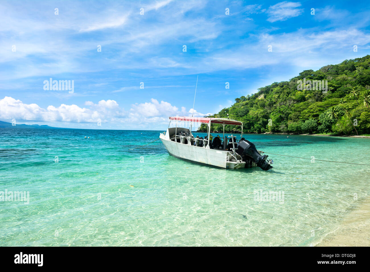 A scuba diving boat anchored in a beautiful tropical bay of turquoise water and a bright, blue vibrant sky with patchy clouds. Stock Photo