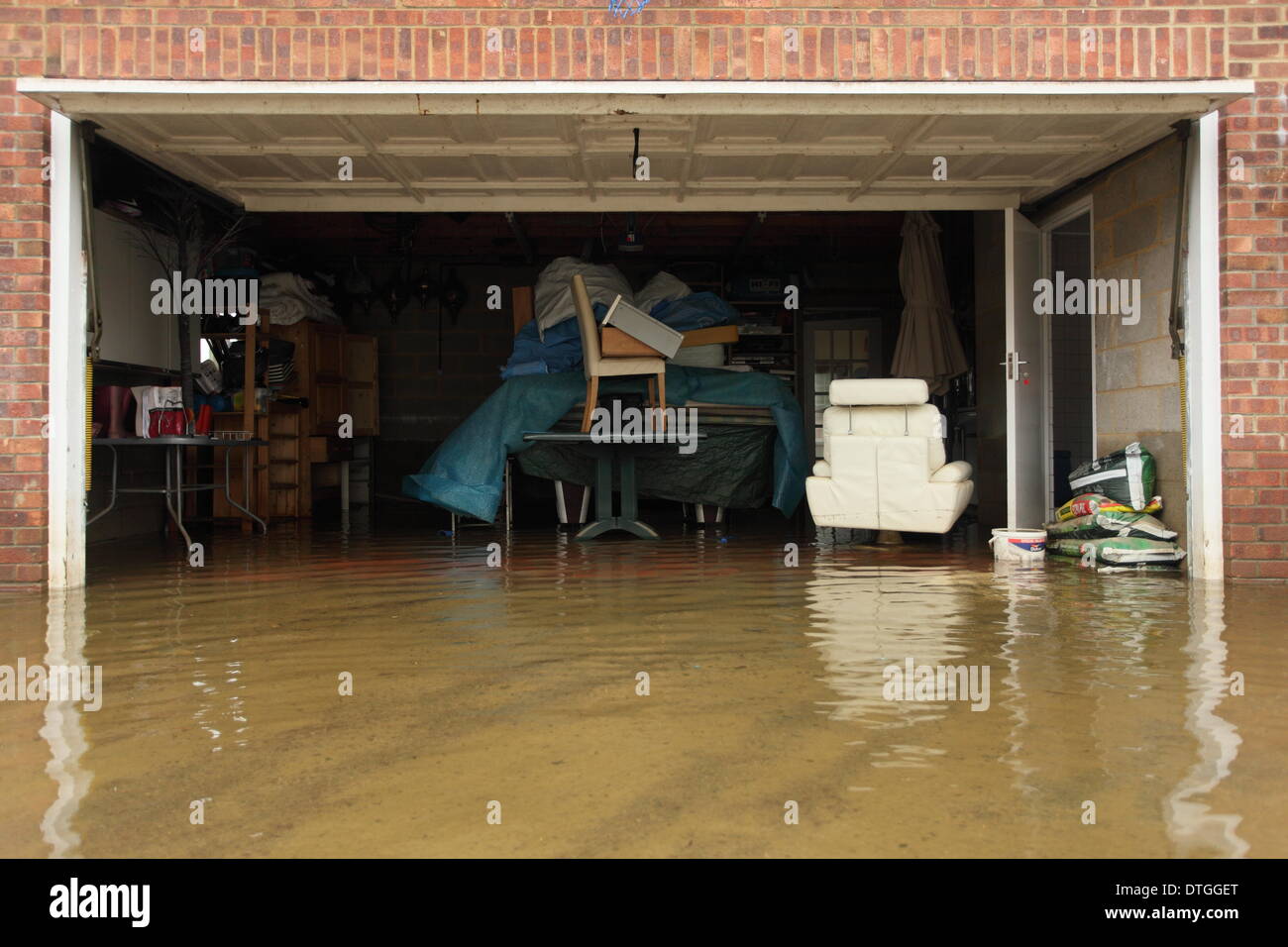 Ham Island, Thames Valley, UK.  Flooded garage with household furniture stacked on tables. Flood waters surround homes and gardens. Stock Photo