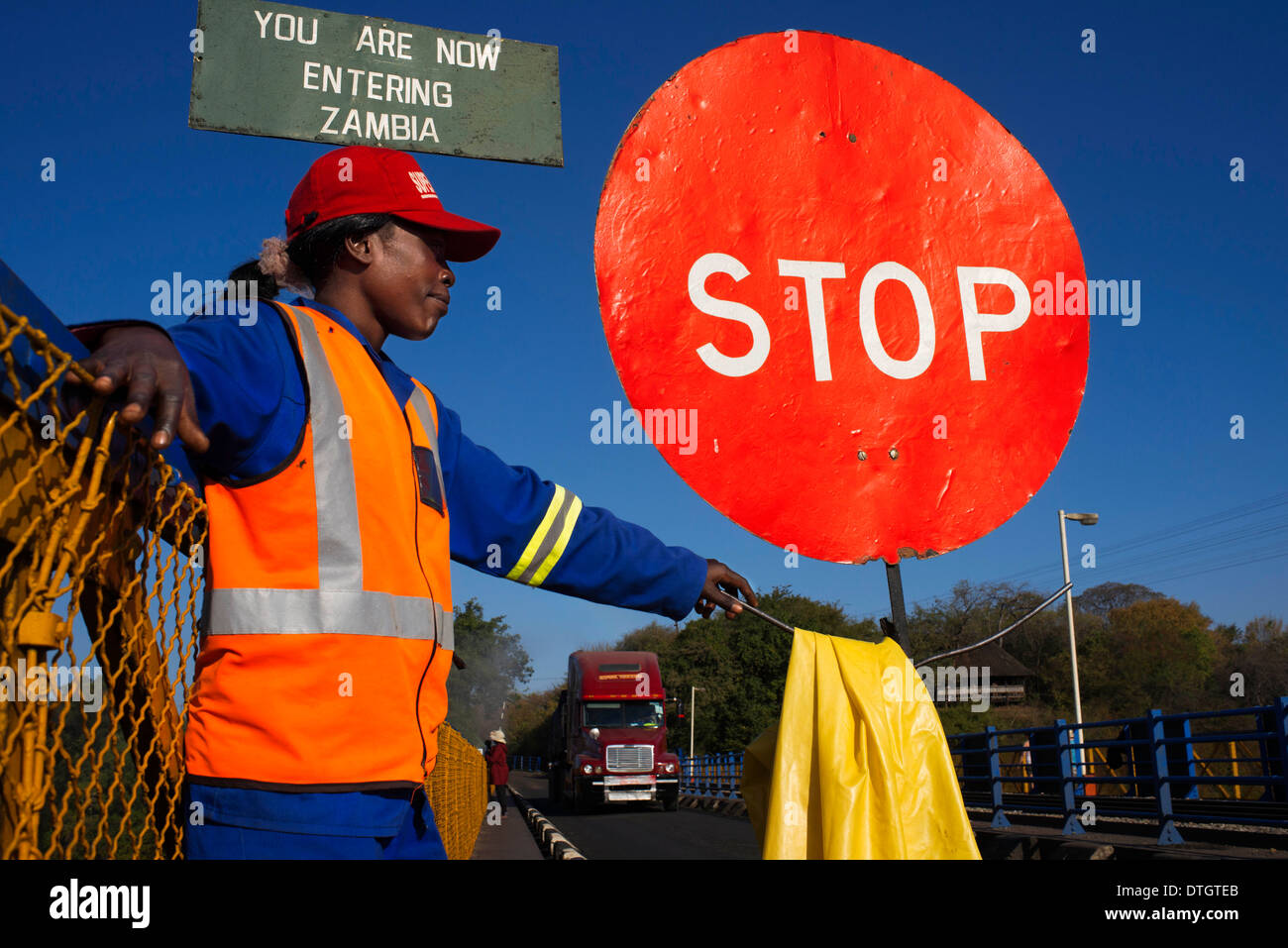 A woman controls the traffic between Zambia and Zimbabwe.  A STOP sign indicates that we are entering Zambia. Stock Photo
