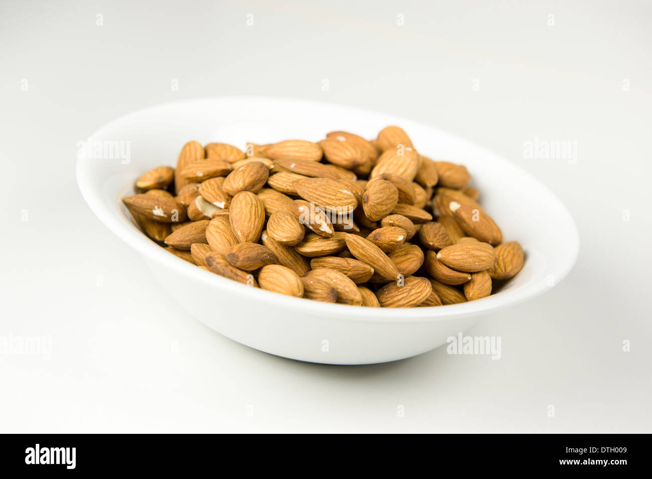 Close up photograph of shelled almonds in a white bowl, on a white background. Stock Photo