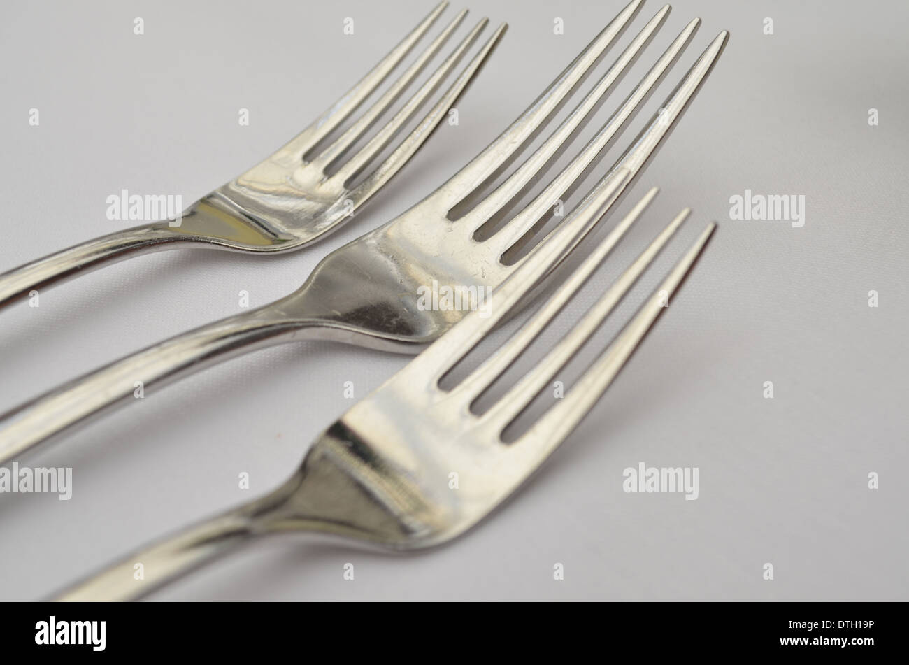 Three silver forks on a white tablecloth Stock Photo