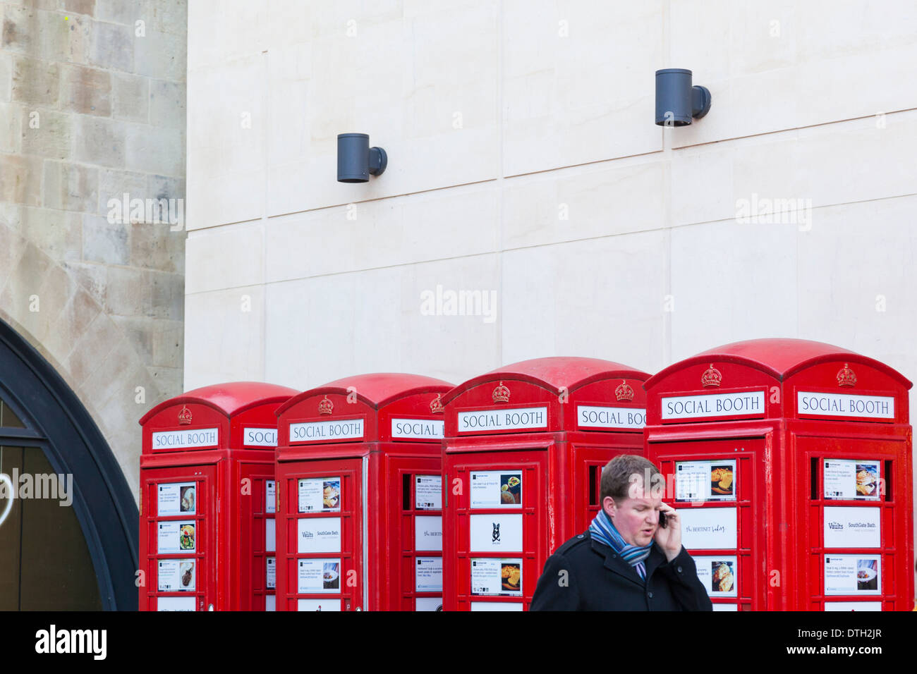 A man make a call on his mobile telephone in front of a row of dummy iconic red telephone boxes. Stock Photo