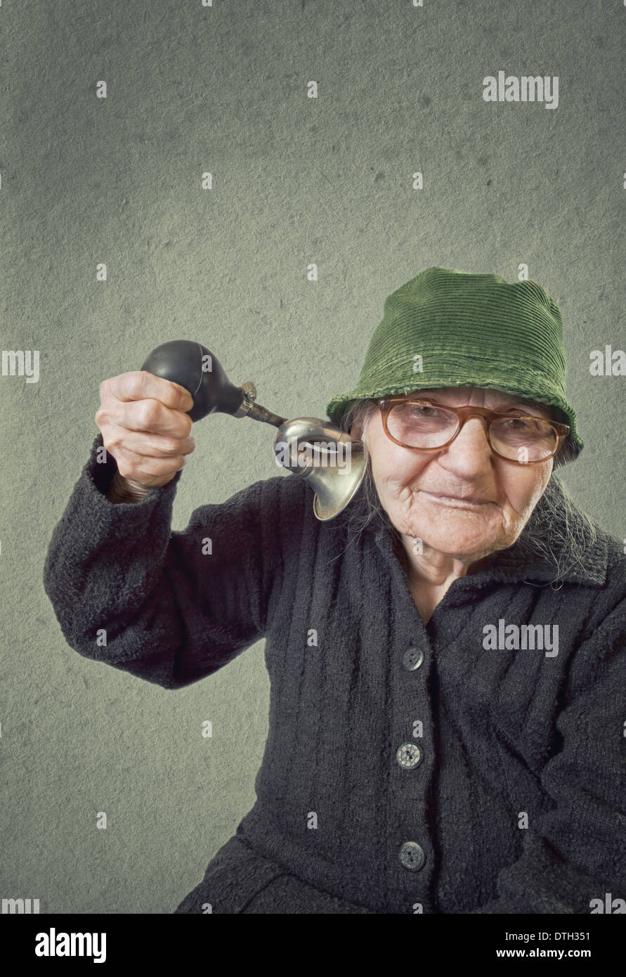 Elderly woman squeezing horn into her own ear on a vintage background. Stock Photo