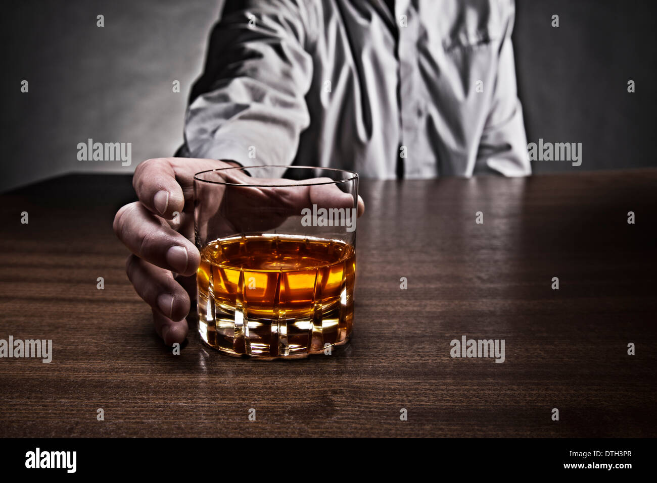 Hand of a man reaching for a glass of whiskey, which stands on a table. Stock Photo