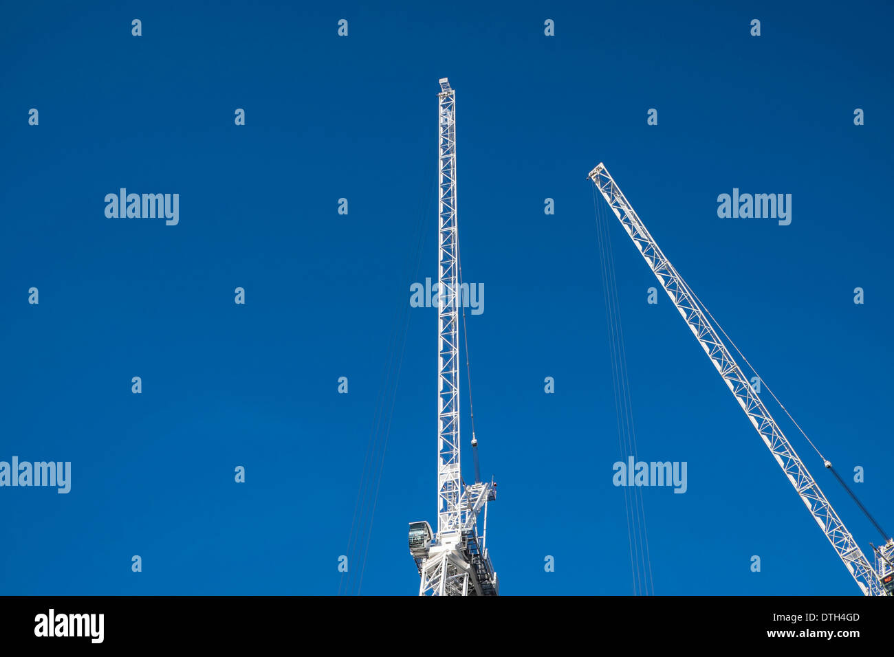 Two white crane angled towards each other against a clear blue sky. Stock Photo