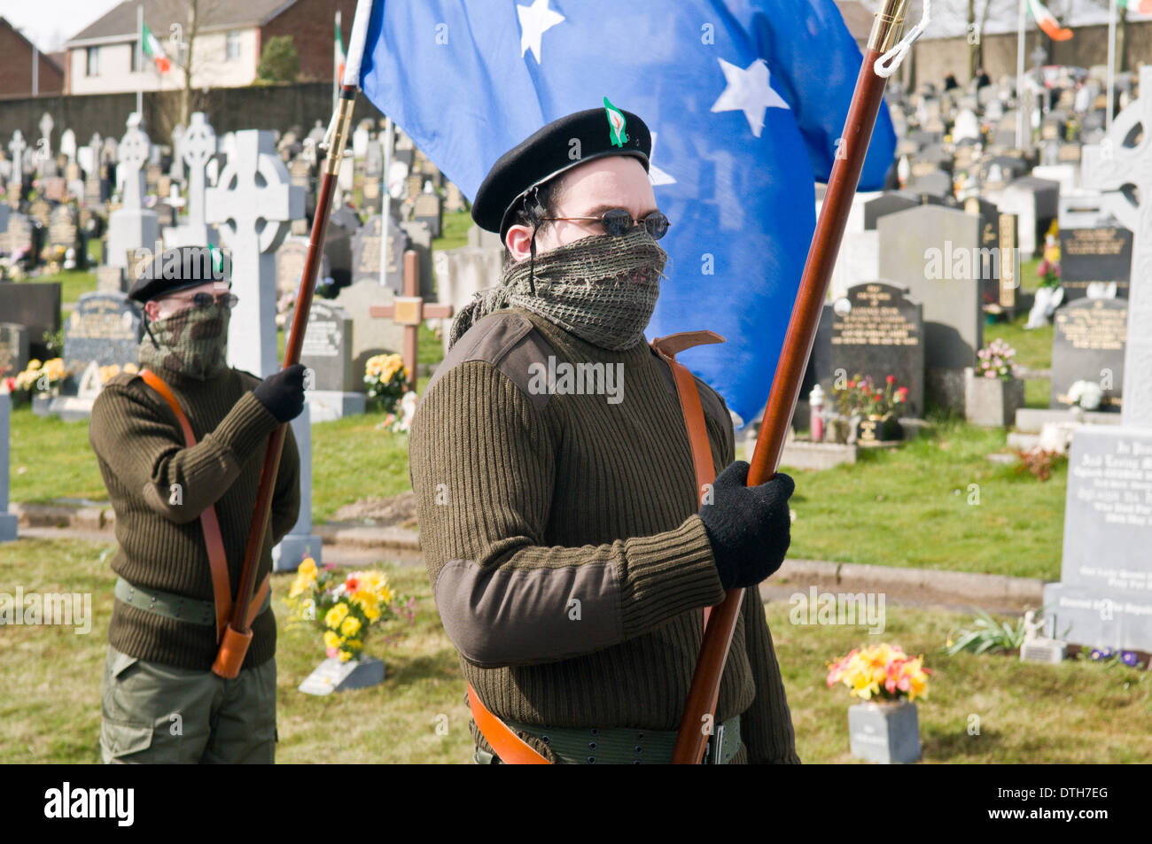 Two men dressed in IRA paramilitary uniforms carry flags at Derry Cemetery Stock Photo