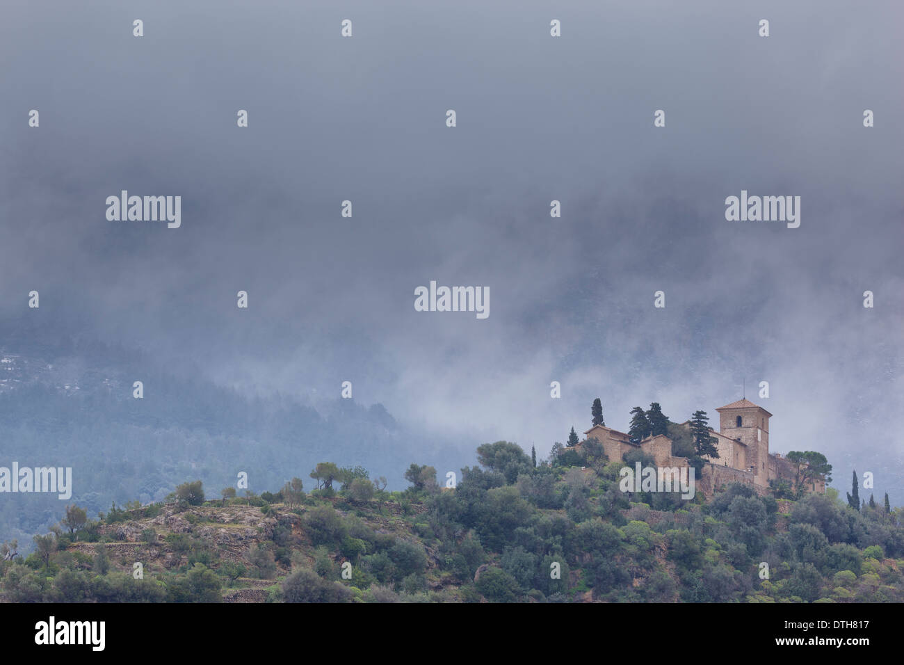 Church of Deià and Tramuntana mountains in the background shrouded in mist. Wintertime. Majorca, Balearic islands, Spain Stock Photo