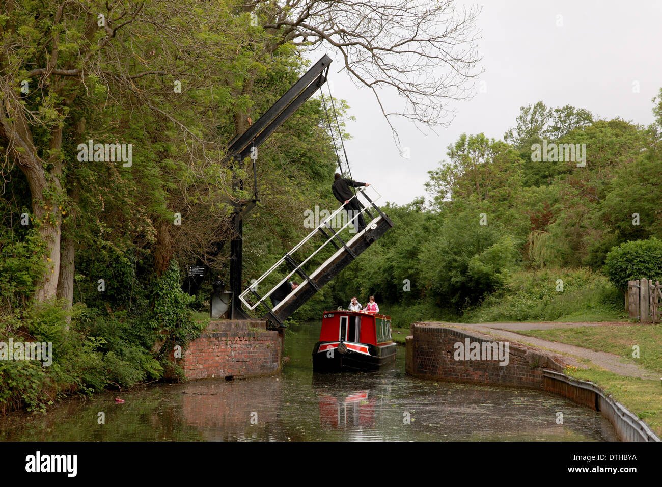 A man standing on the raised lift bridge at Hockley Heath on the Stratford on Avon Canal with a narrowboat underneath Stock Photo