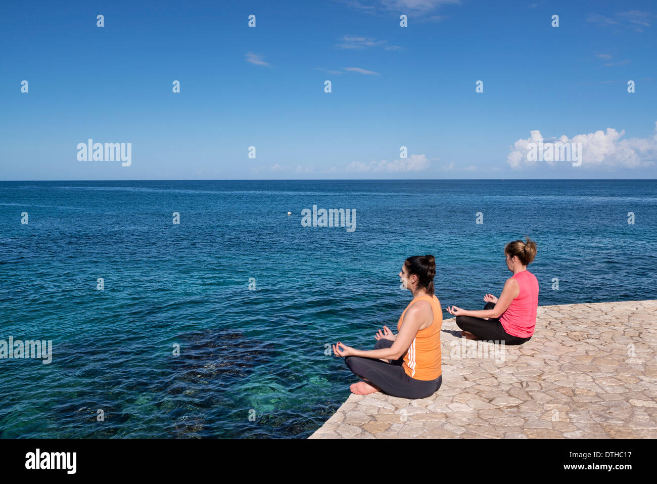 Women practice yoga meditation from an ocean waterfront ledge, Negril, Jamaica. Stock Photo