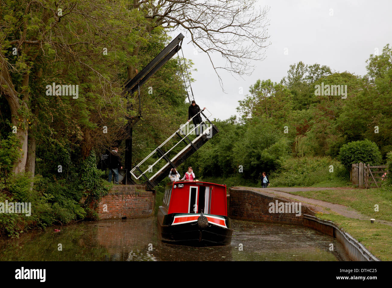 A man standing on the raised lift bridge at Hockley Heath on the Stratford on Avon Canal with a narrowboat underneath Stock Photo