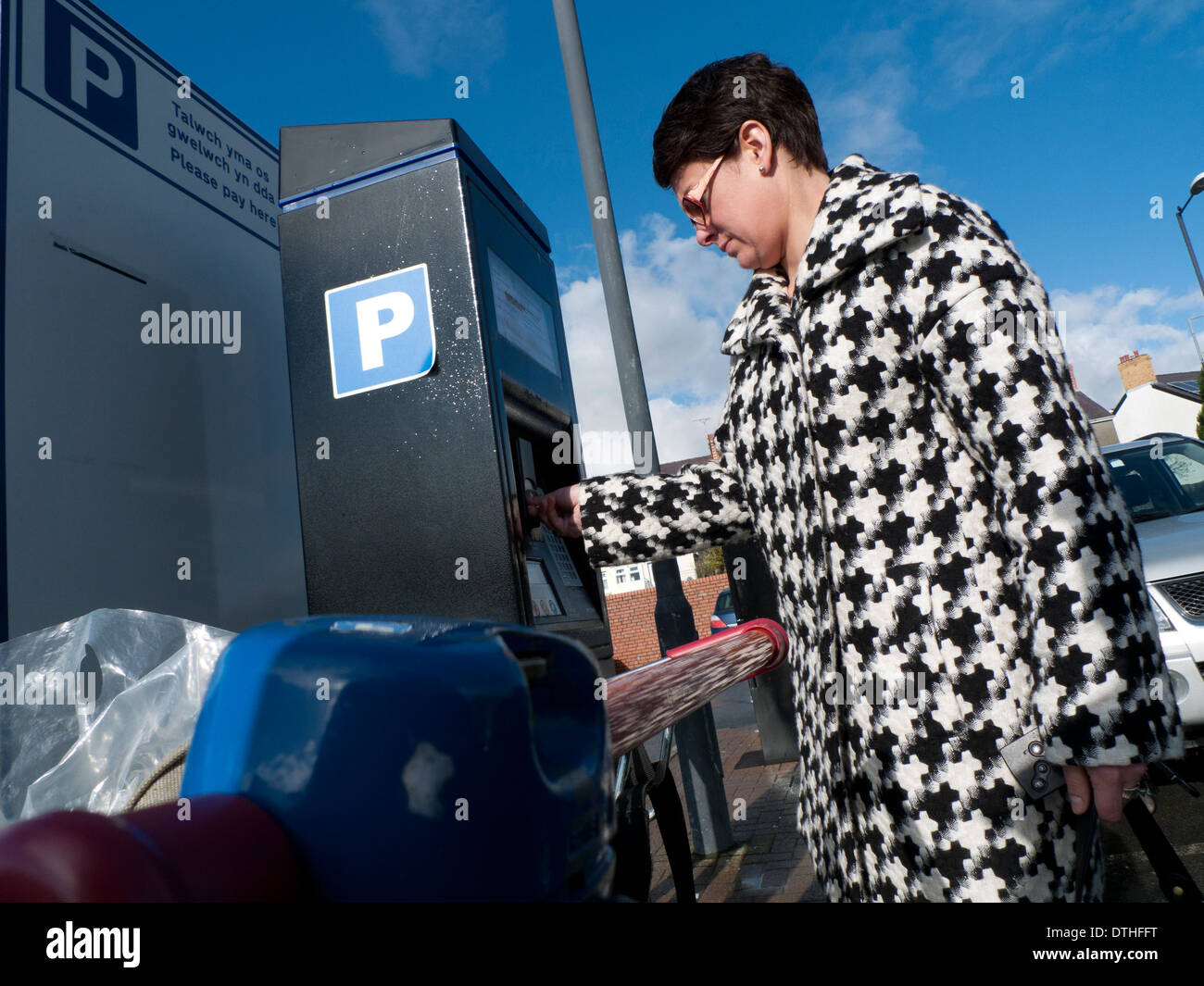 A woman in a houndstooth pattern fabric check coat putting money into a parking machine in a supermarket carpark UK KATHY DEWITT Stock Photo