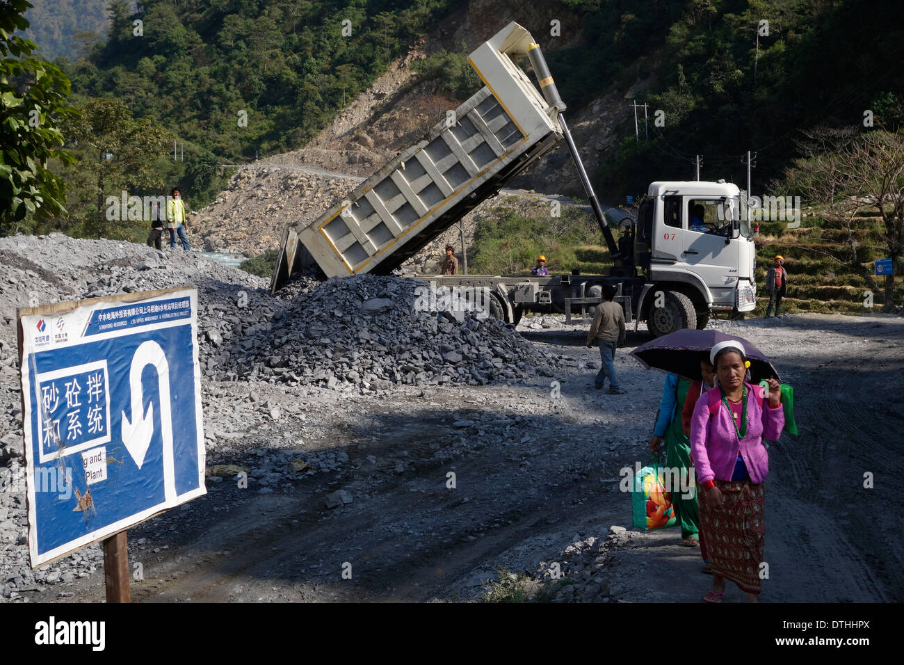 Nepalese women walking by a new cement plant, part of the construction of the Upper Marsyangdi River dam project, Nepal. Stock Photo