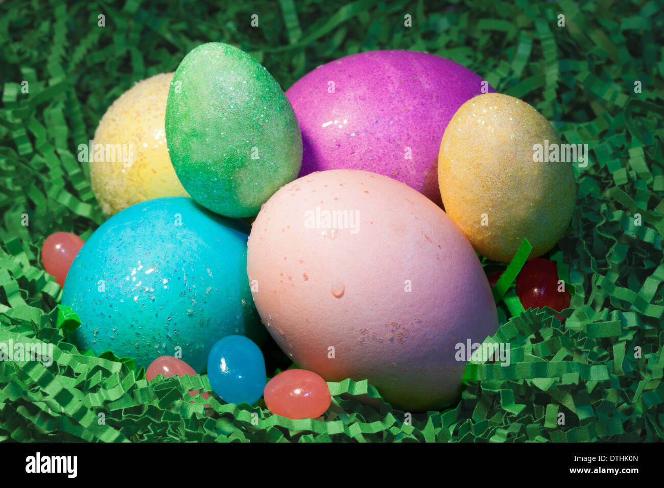 Colored Easter eggs in Easter grass with jelly beans. Stock Photo