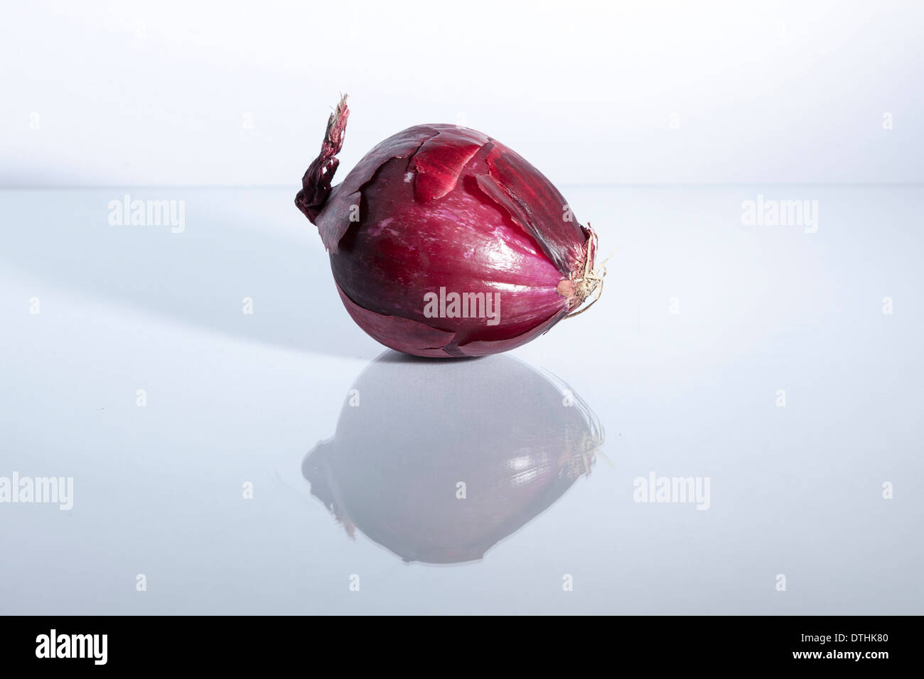 A red onion with skin sitting on it's side with reflection on glass surface of white. Stock Photo